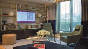 Un salón moderno con un televisor de pantalla plana grande, una estantería, una mesa de centro de cristal y dos sillones.