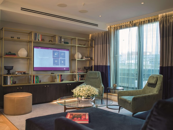 A modern living room with a large flat-screen TV, a bookshelf, a glass coffee table, and two armchairs. - The Guardsman Hotel and Residences (London)