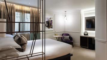A hotel room with a bed, a desk, a chair, a TV, and a window with curtains.