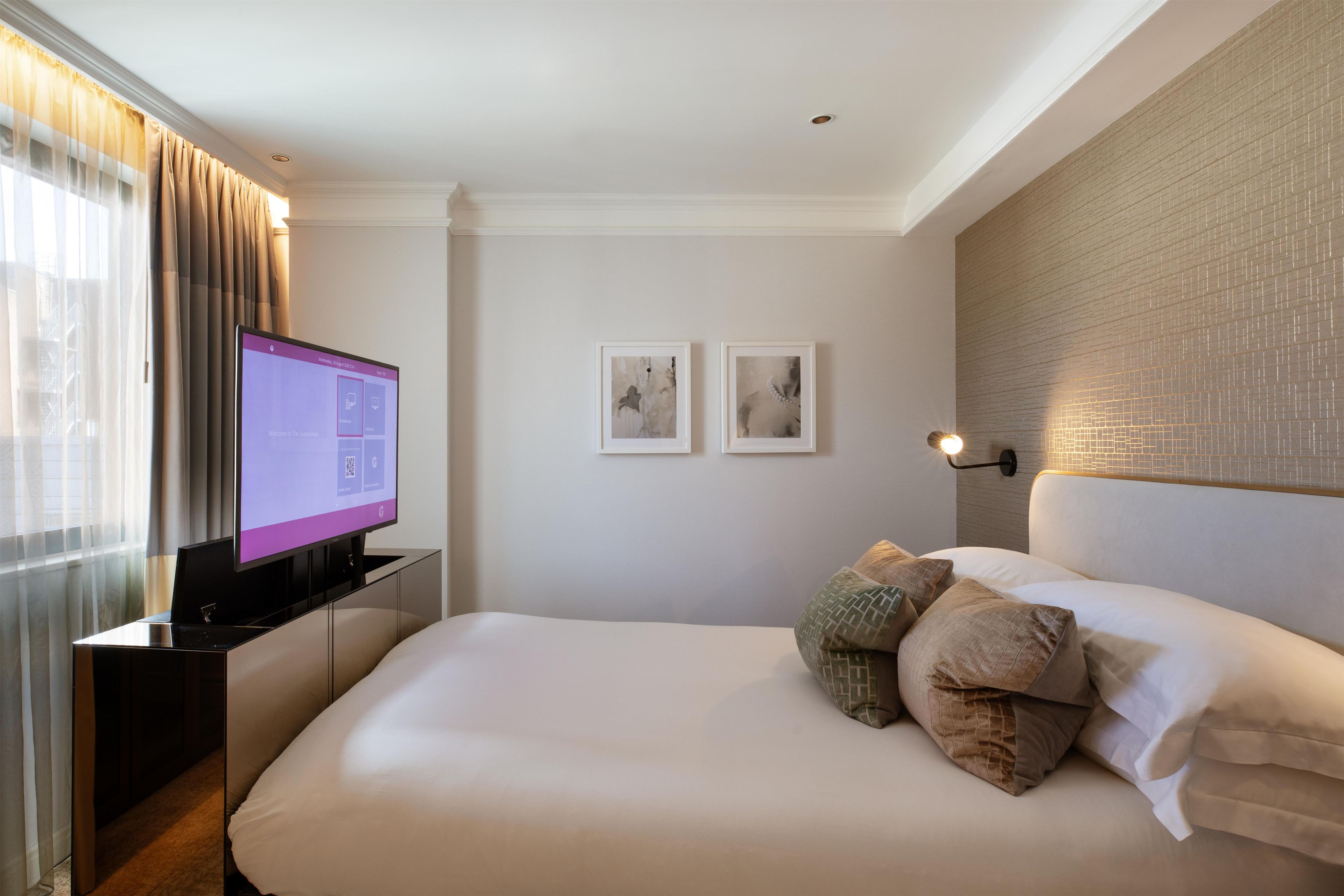 Una habitación de hotel con una cama, un televisor sobre un mueble bajo, una pared con dos cuadros enmarcados y una pared con diseño de ladrillo.