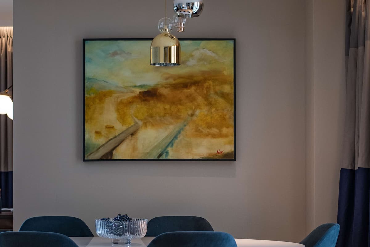 Uma sala de jantar com mesa e cadeiras, um quadro na parede e um lustre.