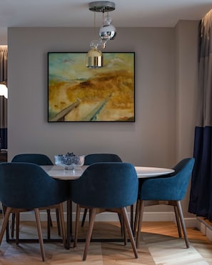 A dining area with a table and chairs, a painting on the wall, and a hanging light fixture. - The Guardsman Hotel and Residences (London)