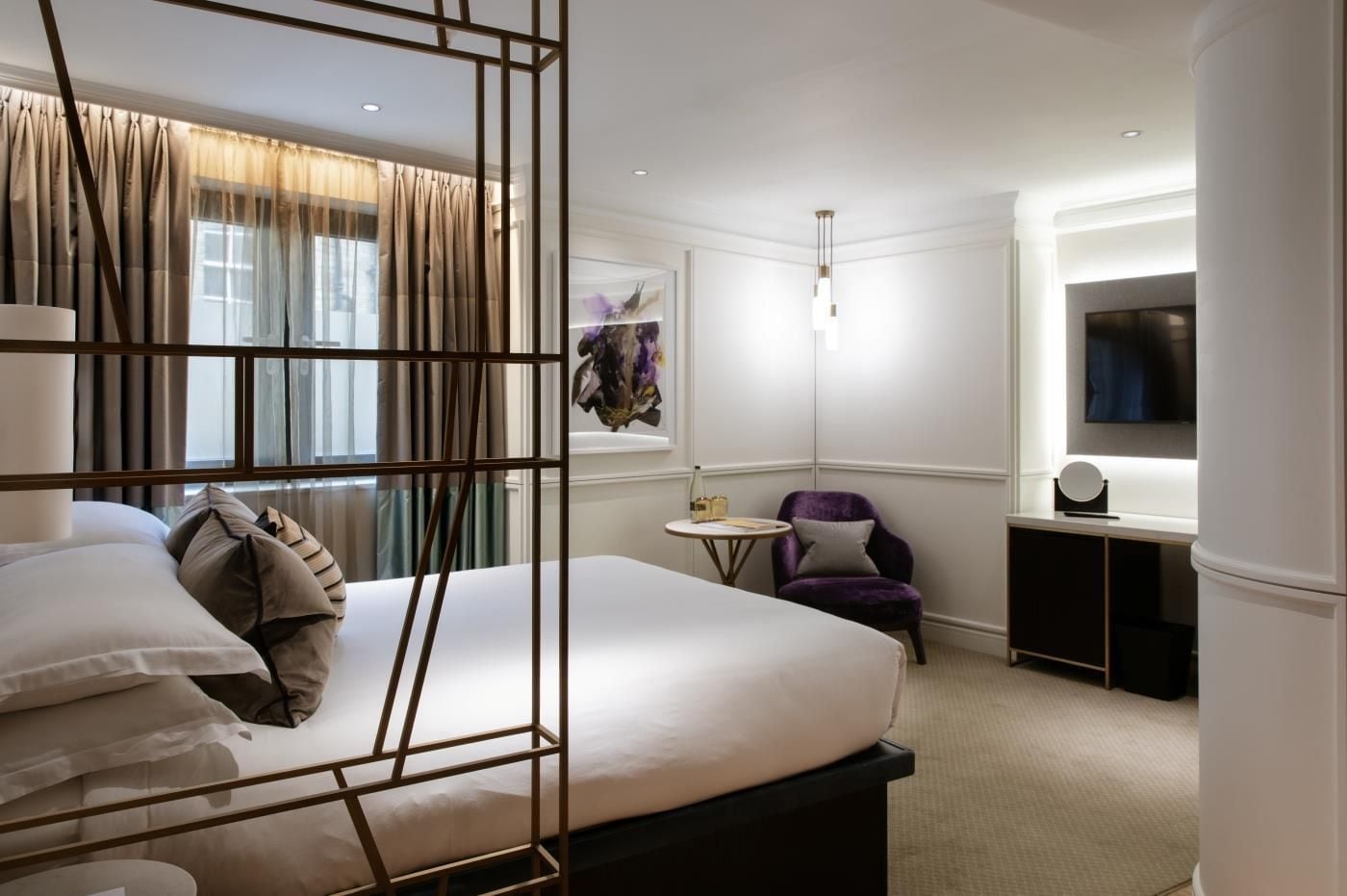 Une chambre d’hôtel avec un grand lit, une petite table ronde, un fauteuil violet, une télévision et un tableau au mur.
