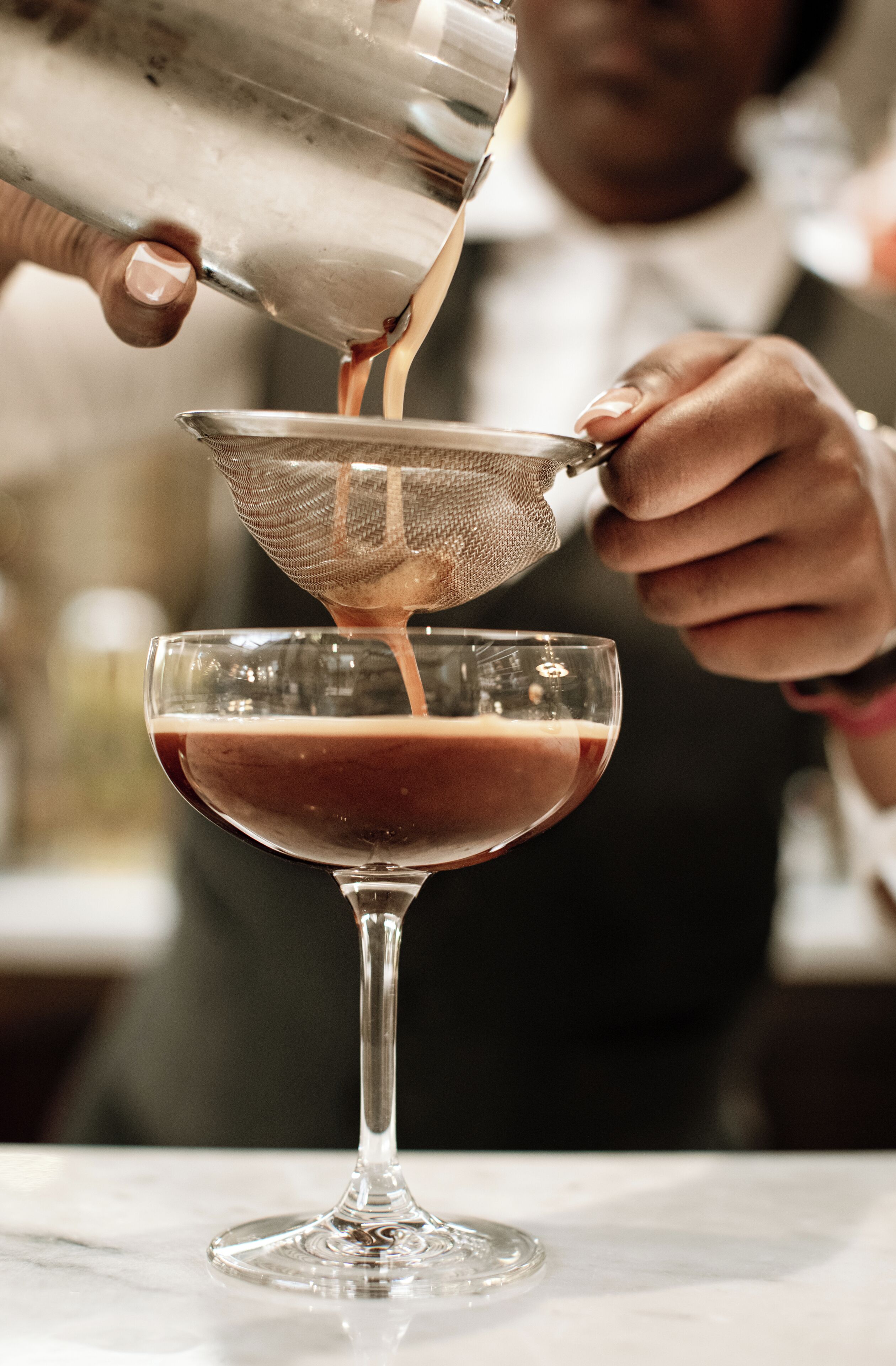 A person pouring a liquid into a glass with a strainer.