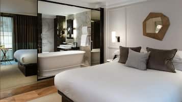 Habitación de hotel moderna con una cama grande, una bañera y un separador de vidrio.