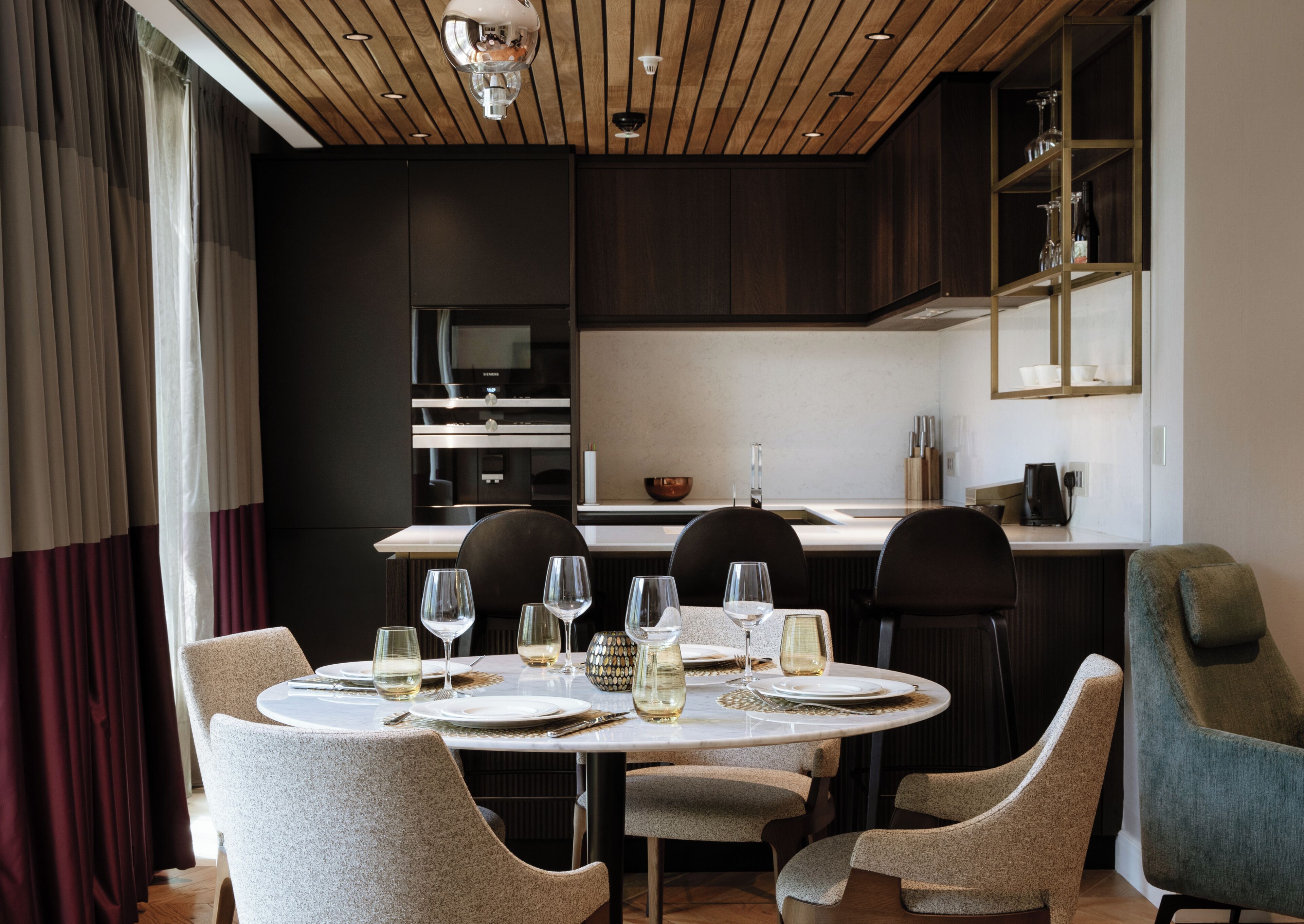 A modern dining area with a round table set for six, equipped with wine glasses and plates.
