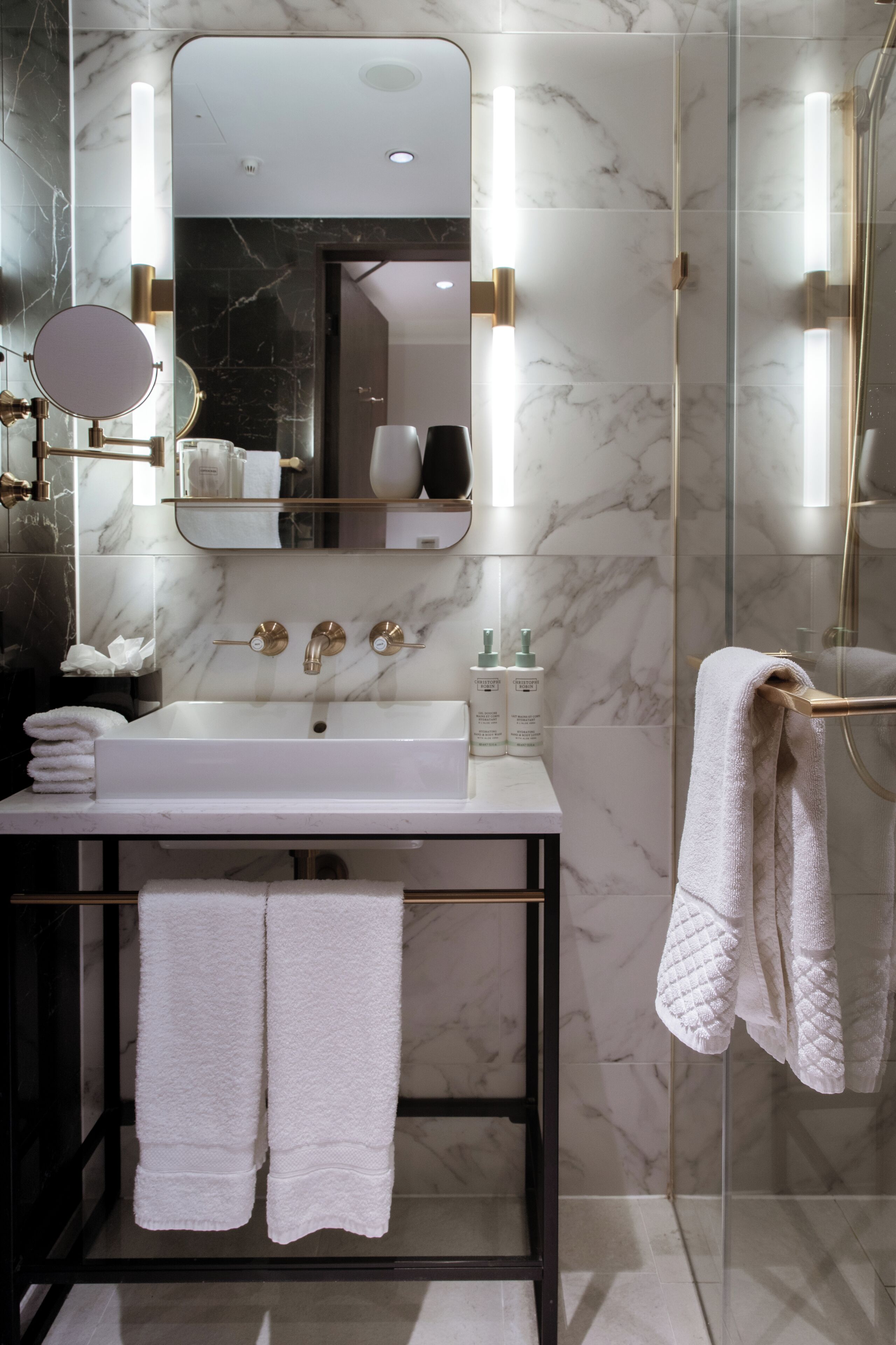 A modern bathroom with a marble sink, a large mirror, and a glass shower enclosure.