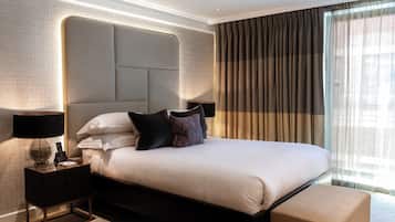 A hotel room with a large bed, a headboard, a bedside table with a lamp, and a window with curtains.