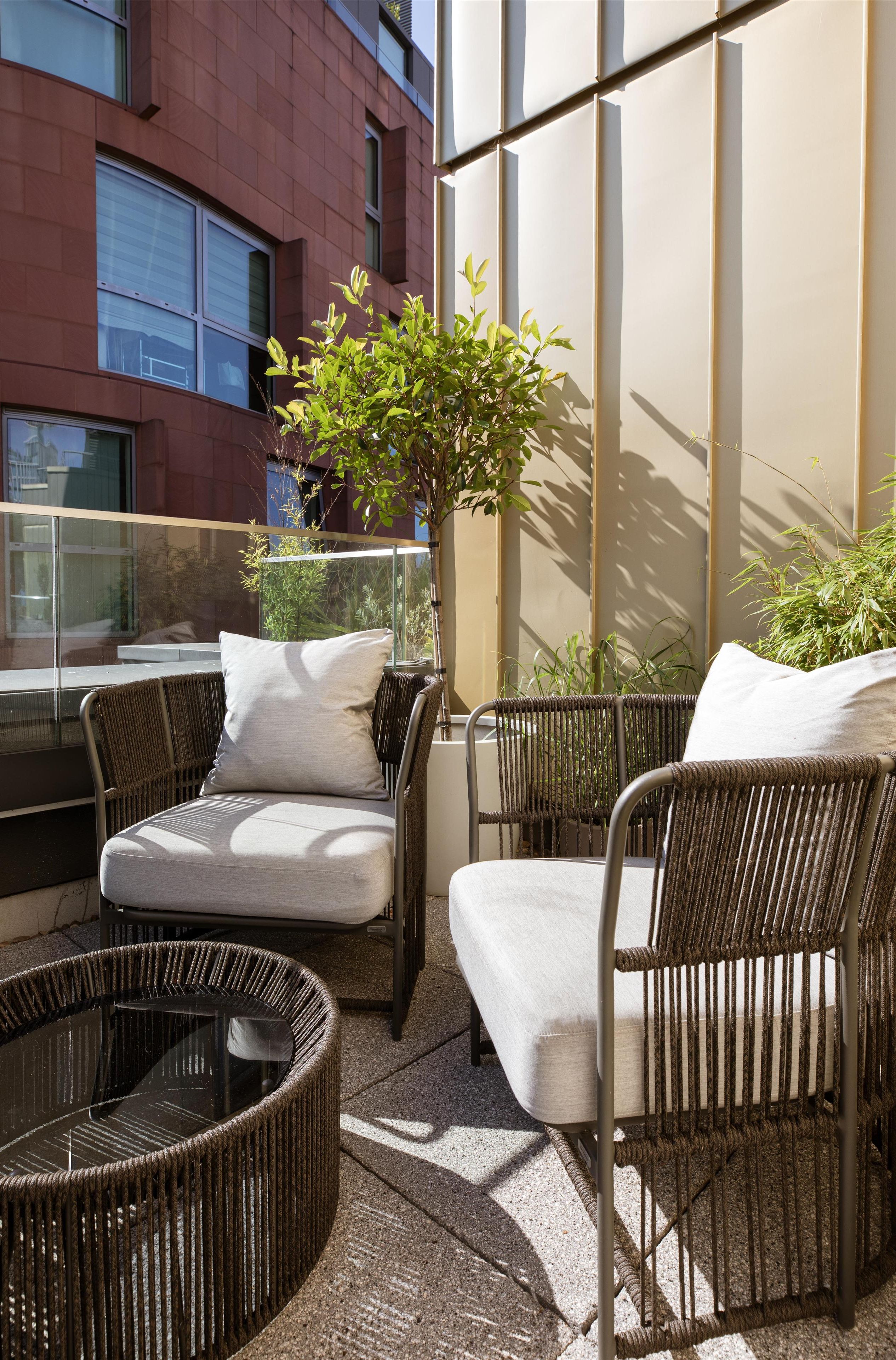 A balcony with wicker furniture, a potted plant, and a view of a building.