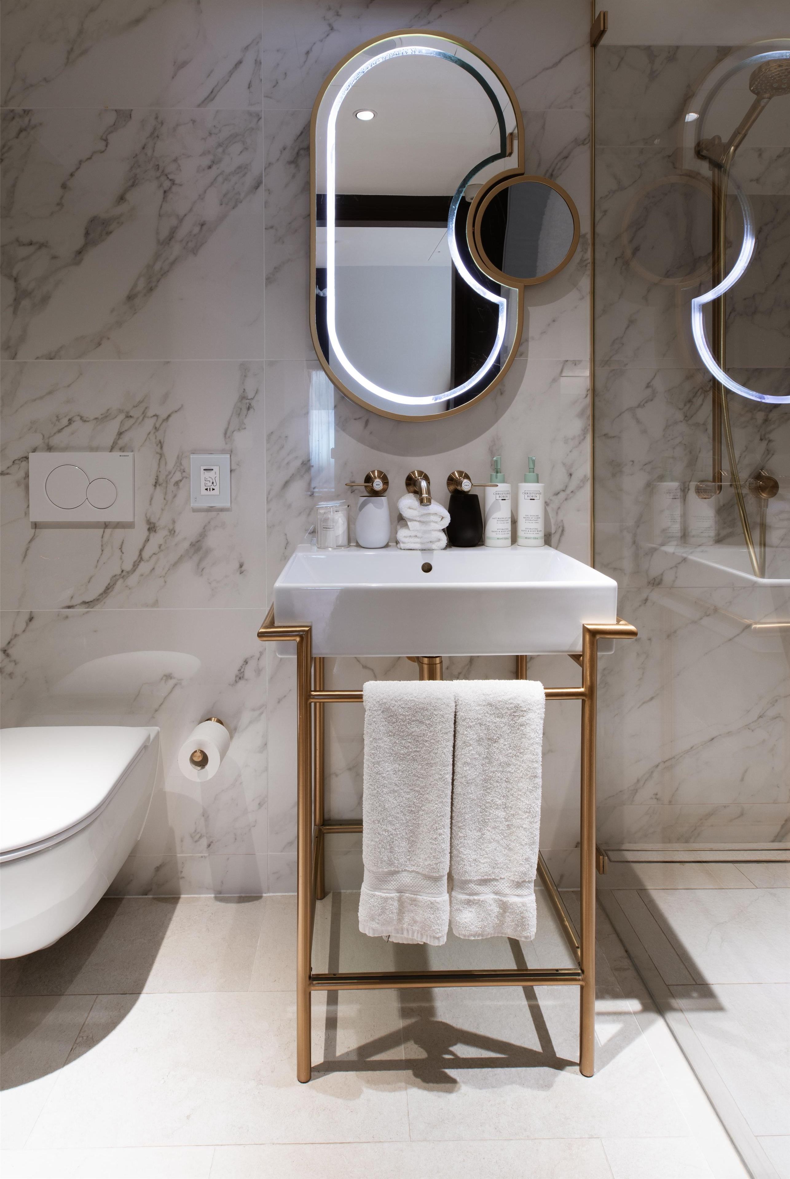 A bathroom with a white marble sink, gold fixtures, and a large mirror with integrated lighting.