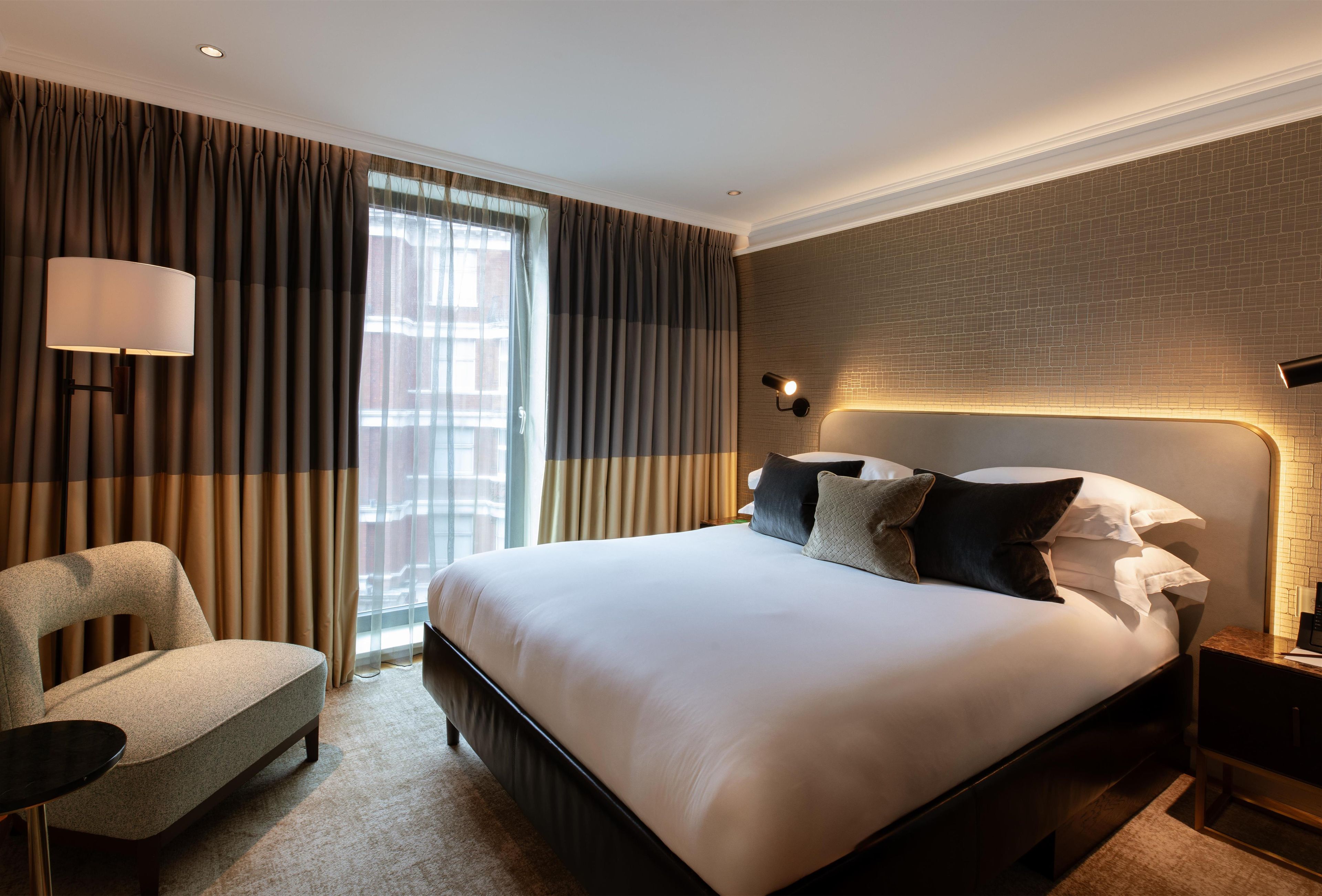 A hotel room with a large bed, a chair, a desk, and a window with curtains.