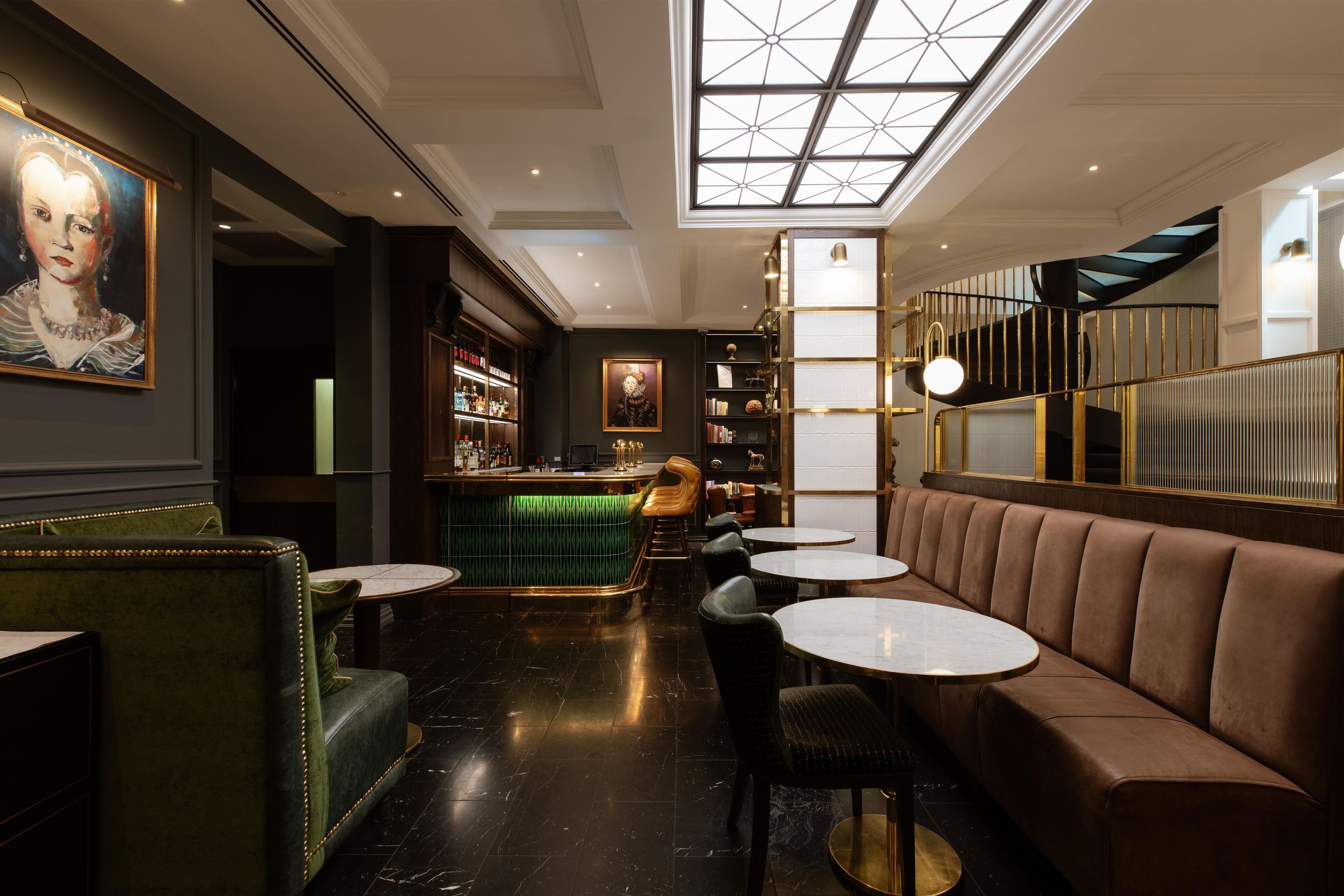 A bar area with a high ceiling, a green bar counter, and seating with round tables and cushioned booths.