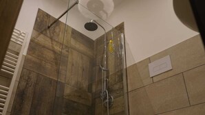 Une douche avec un espace clos en verre, une douchette à main et un panneau de commande fixé au mur.