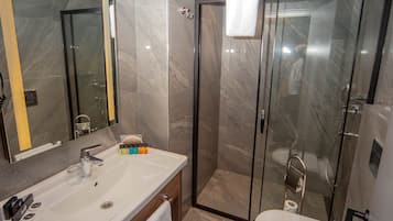 Un baño moderno con un espejo grande, un lavamanos, un inodoro y una ducha con cerramiento de vidrio.