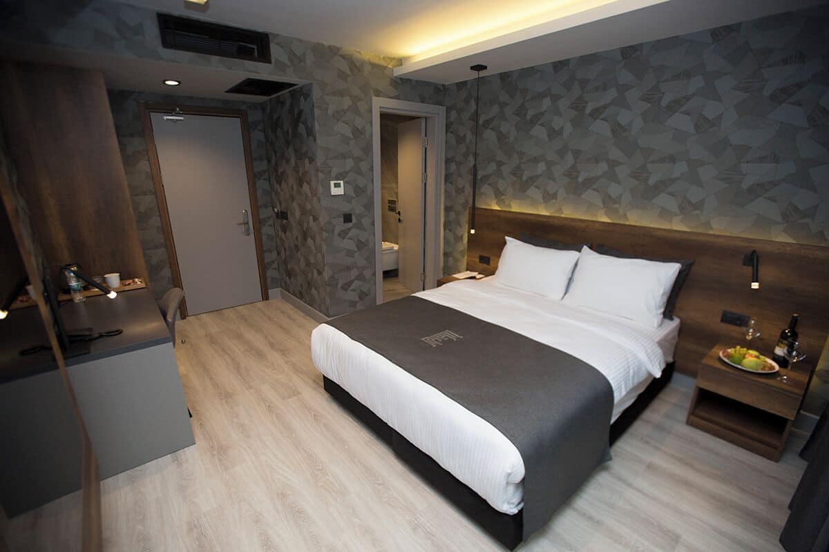 A modern hotel room with a large bed, a wooden nightstand, and a desk with a chair.