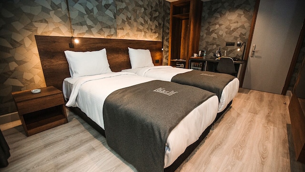 A hotel room with two beds, a wooden headboard, a desk, and a wardrobe. - Emens Hotel (Izmir)