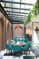 A restaurant with a brick wall, green velvet chairs, and a glass ceiling.
