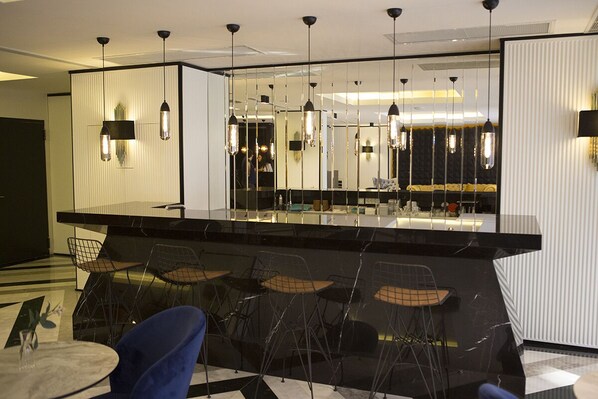 Zona de bar moderna con superficie reflectante, sillas negras e iluminación colgante.