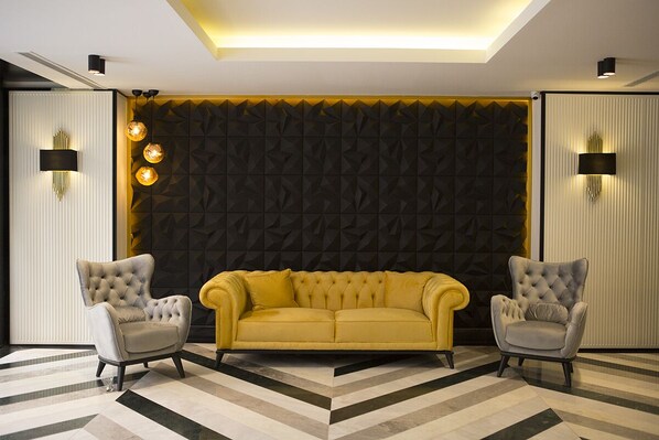 Una sala de estar moderna con un sofá amarillo, dos sillones y un papel tapiz con estampado geométrico.