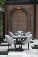 A brick wall with an arched doorway, a table with six chairs, and a hanging light fixture.