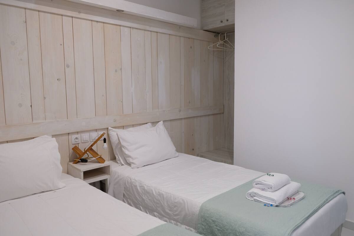 Une chambre d’hôtel avec deux lits, une tête de lit en bois, du linge de lit blanc et un plaid vert.
