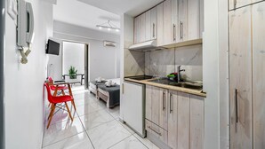 Una cocina moderna con armarios de madera, estufa empotrada y un lavamanos. Hay un comedor con sillas rojas y una mesa pequeña.