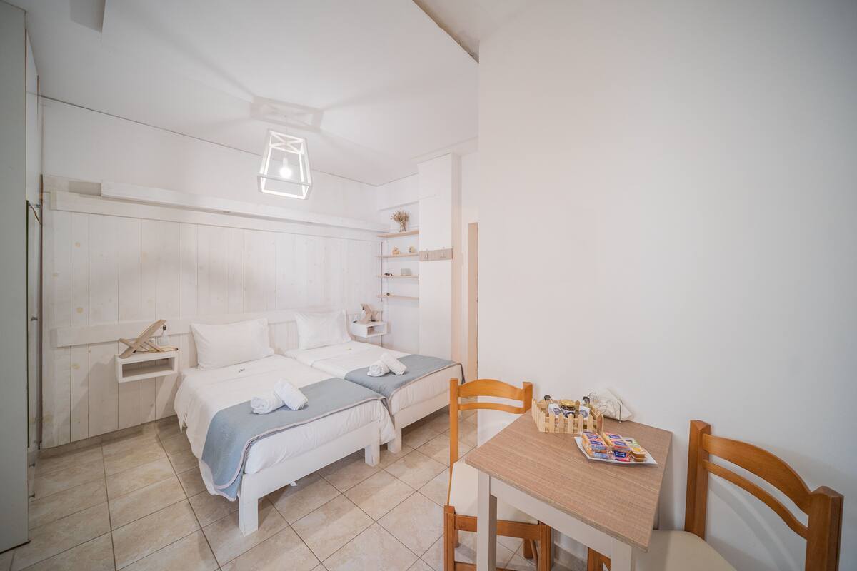 Une chambre avec deux lits, une table en bois avec le petit-déjeuner, et une petite étagère avec des articles de toilette.