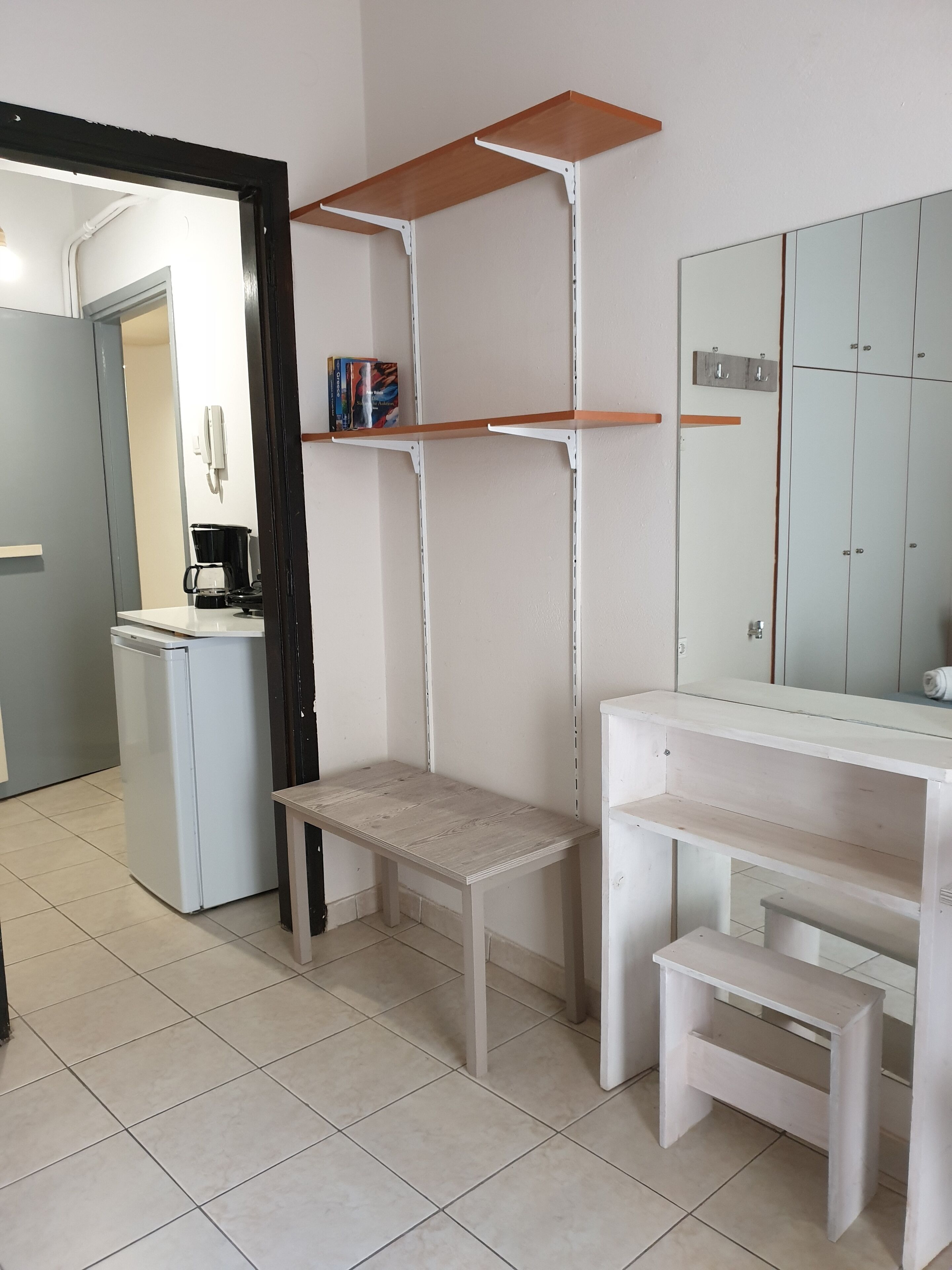 A room with a kitchenette, a small table, a bench, and a wardrobe.