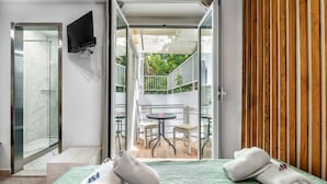 Una habitación de hotel con cama, baño con ducha y balcón con mesa y sillas.