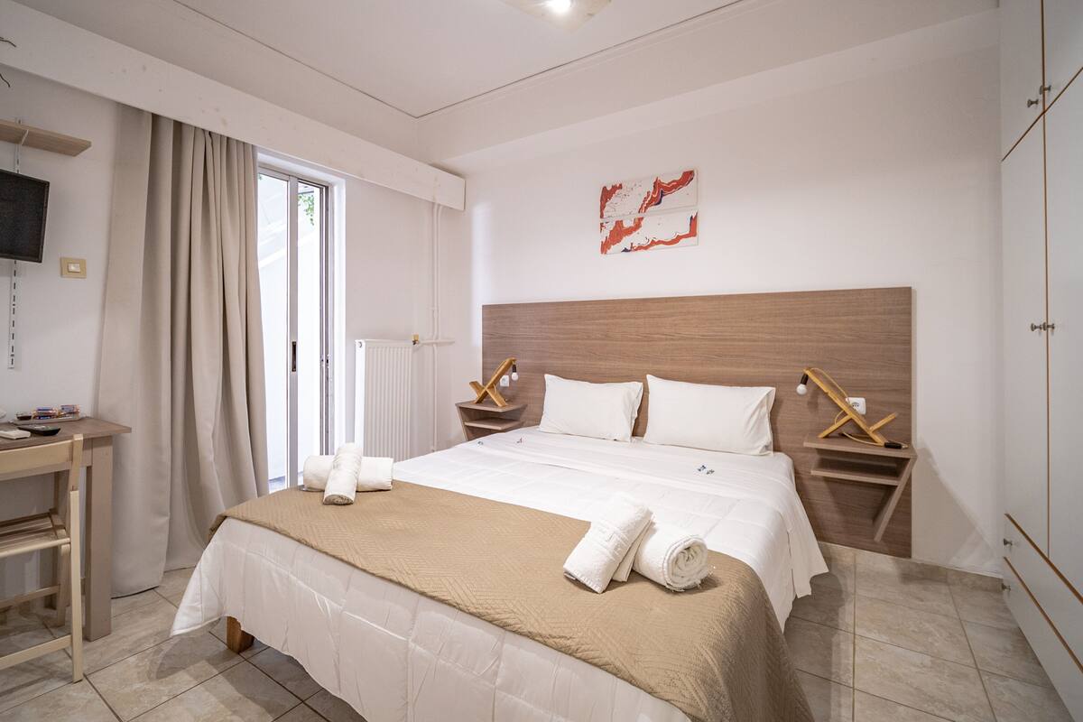 Une chambre d’hôtel moderne avec un grand lit, une tête de lit en bois, un bureau et un téléviseur fixé au mur.