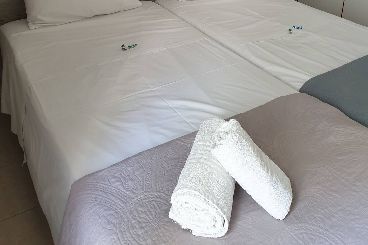 Un lit double avec du linge de lit blanc, une tête de lit en bois, une table de chevet avec une lampe et une serviette soigneusement pliée posée sur le lit.