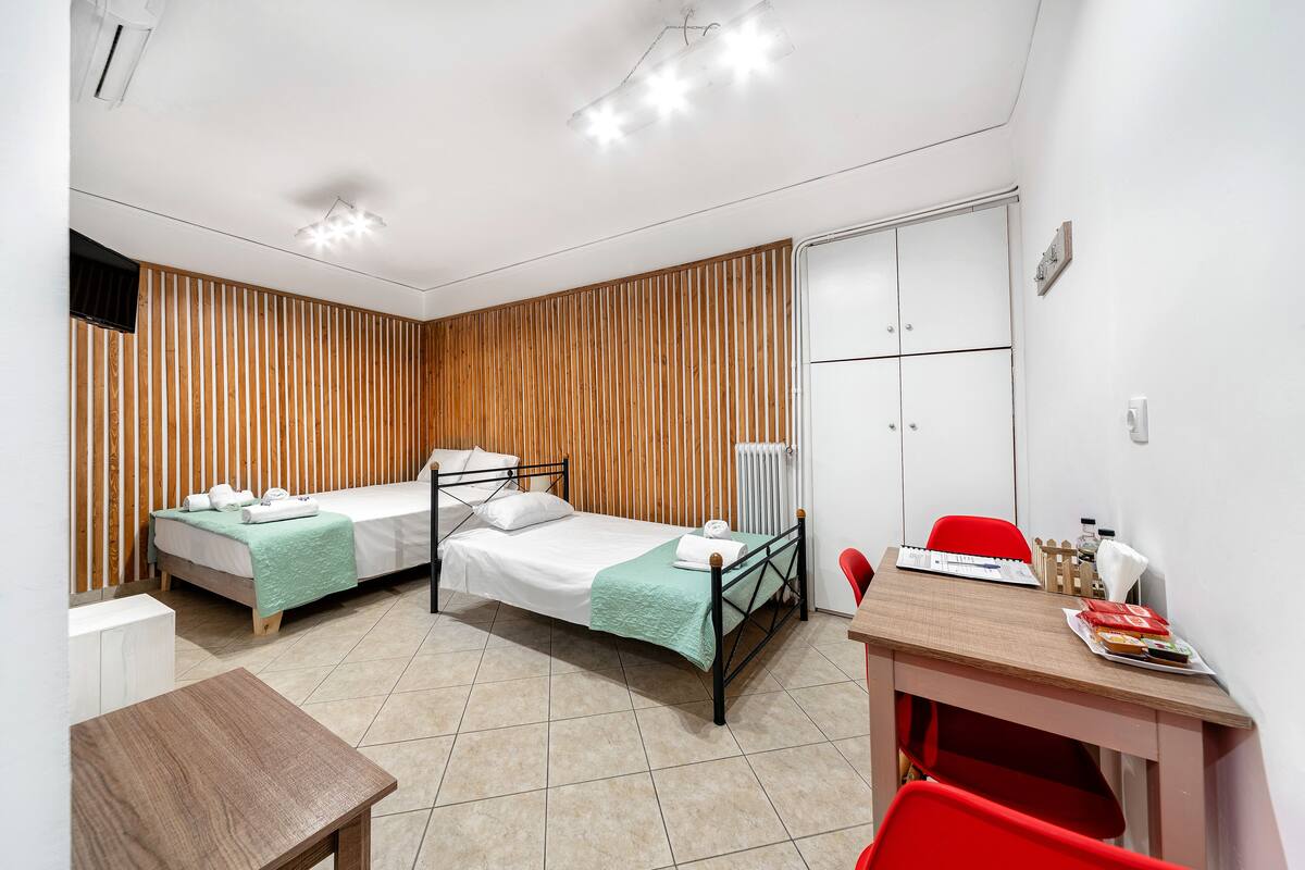 Une chambre d’hôtel avec deux lits, un mur recouvert de lambris en bois, un bureau avec une chaise et un radiateur.