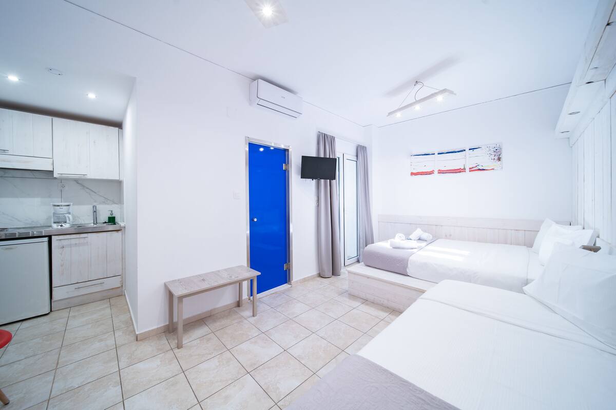 Une chambre d’hôtel moderne équipée d’une kitchenette, d’une porte bleue, d’un lit et d’un téléviseur à écran plat.