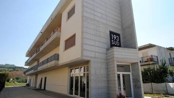 Edificio a più piani con un balcone al secondo piano, un'ampia vetrata d'ingresso e una targa con il numero civico indicato.