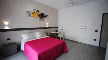 Una camera d'albergo con un letto, una scrivania, una sedia e un quadro appeso al muro.