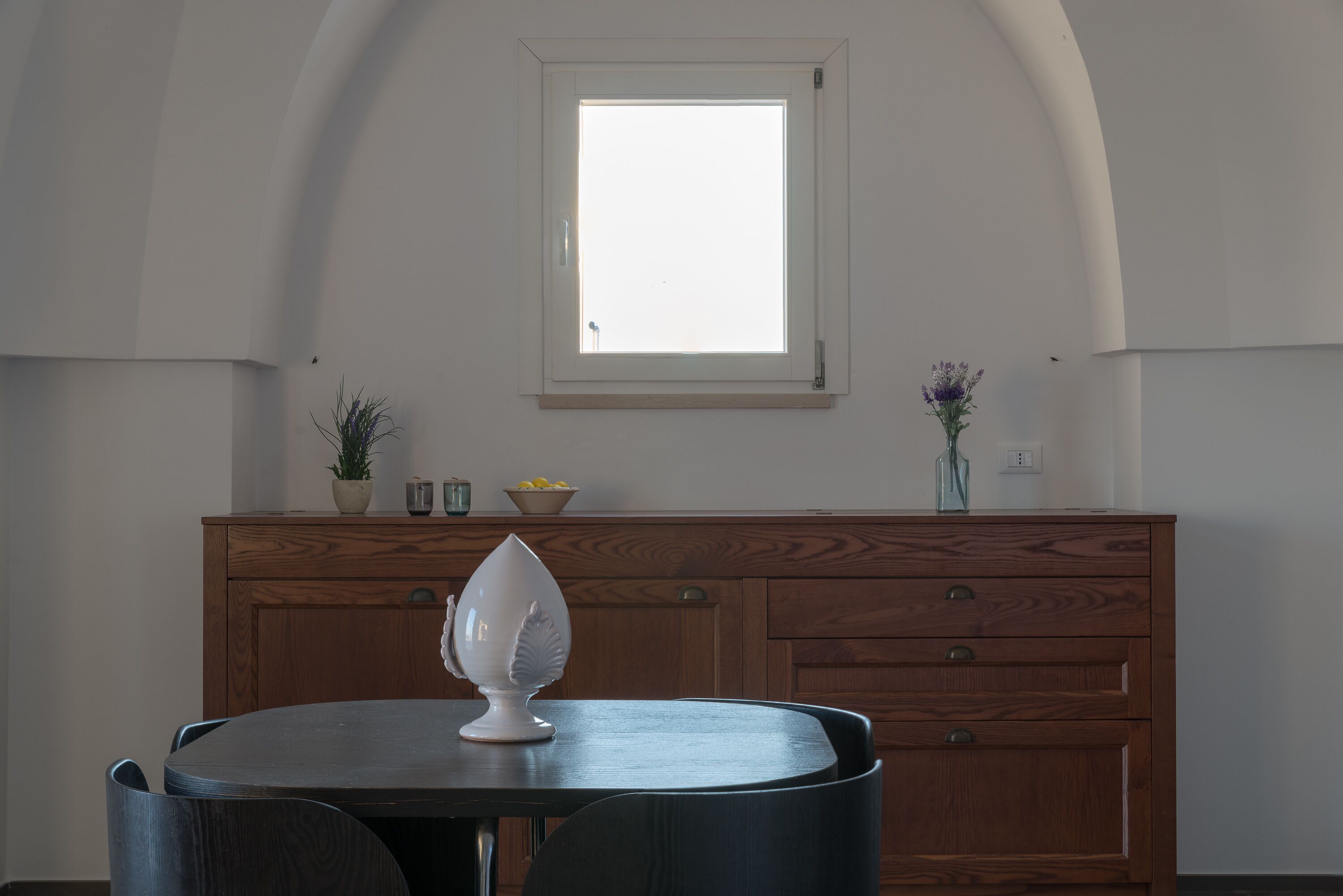 A dining area with a round table, chairs, a wooden cabinet, and a window with a view.