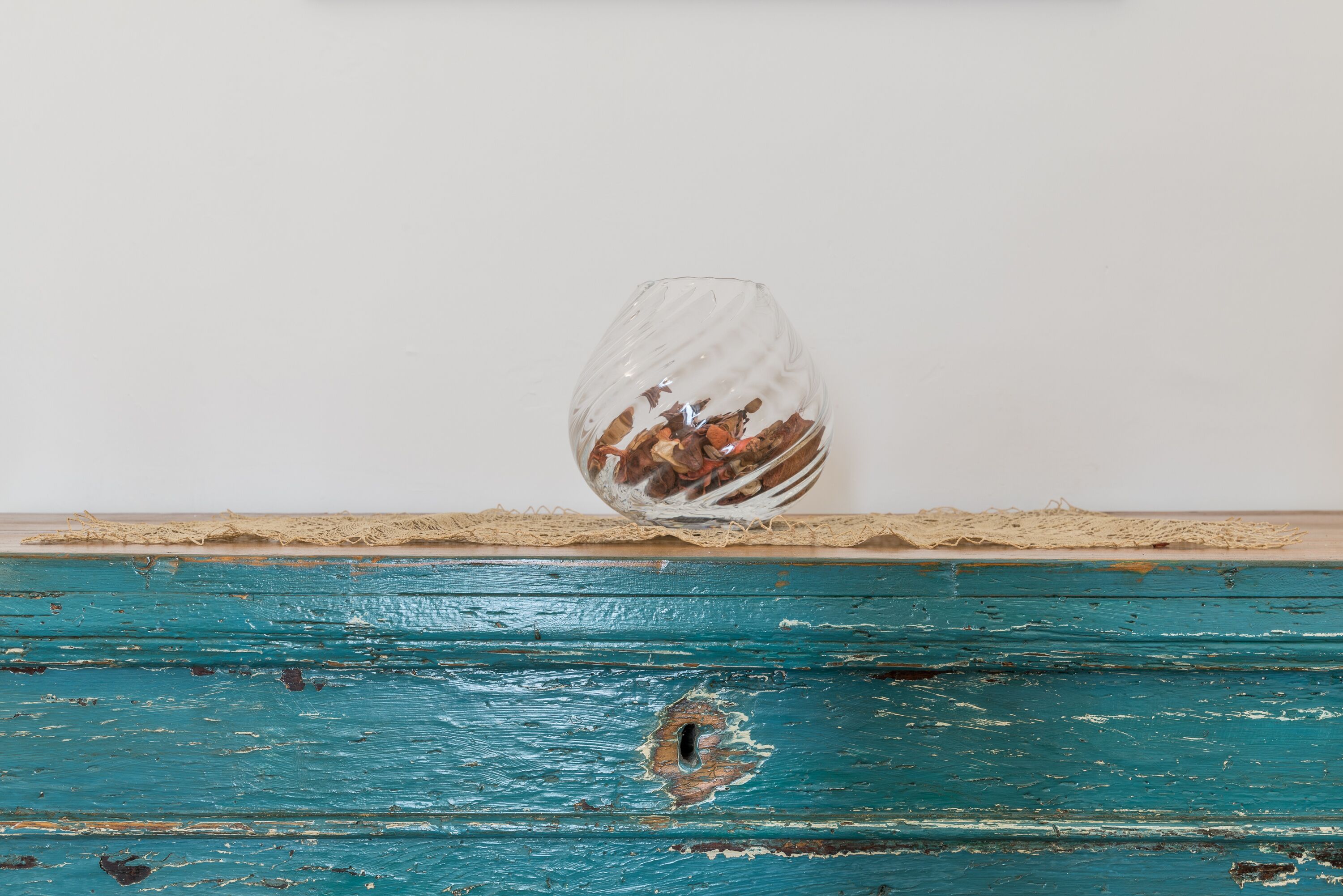 Un florero de vidrio con un diseño texturizado, sobre una superficie de madera con acabado en pintura azul verdoso desgastado.