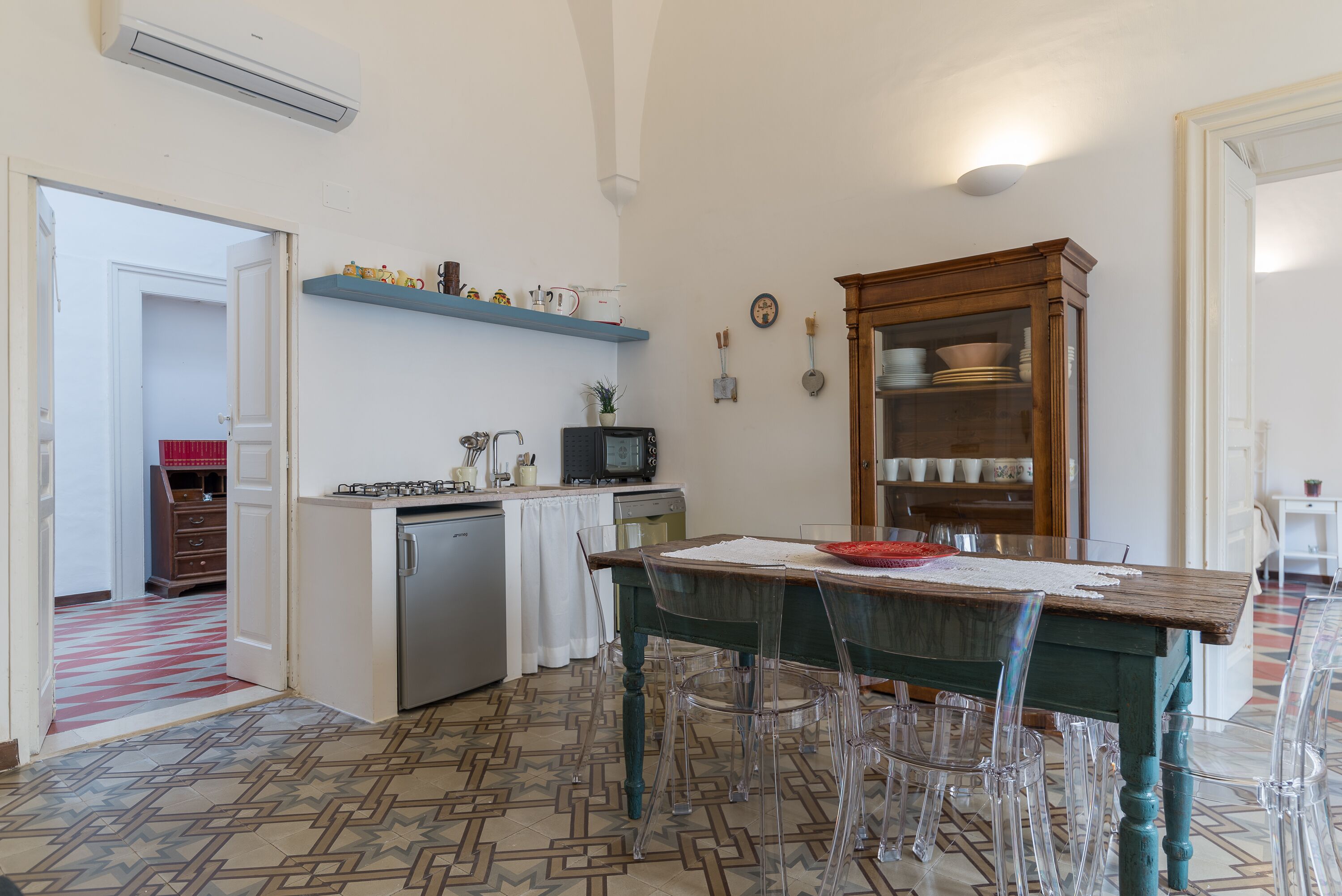 Una cocina con una mesa de madera, sillas transparentes, un microondas y un lavavajillas.