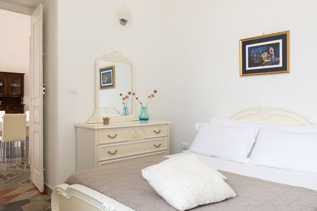 A bedroom with a bed, a dresser, a mirror, and a framed picture on the wall.