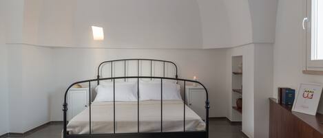Un dormitorio con cama, mesita de noche, escritorio y ventana.