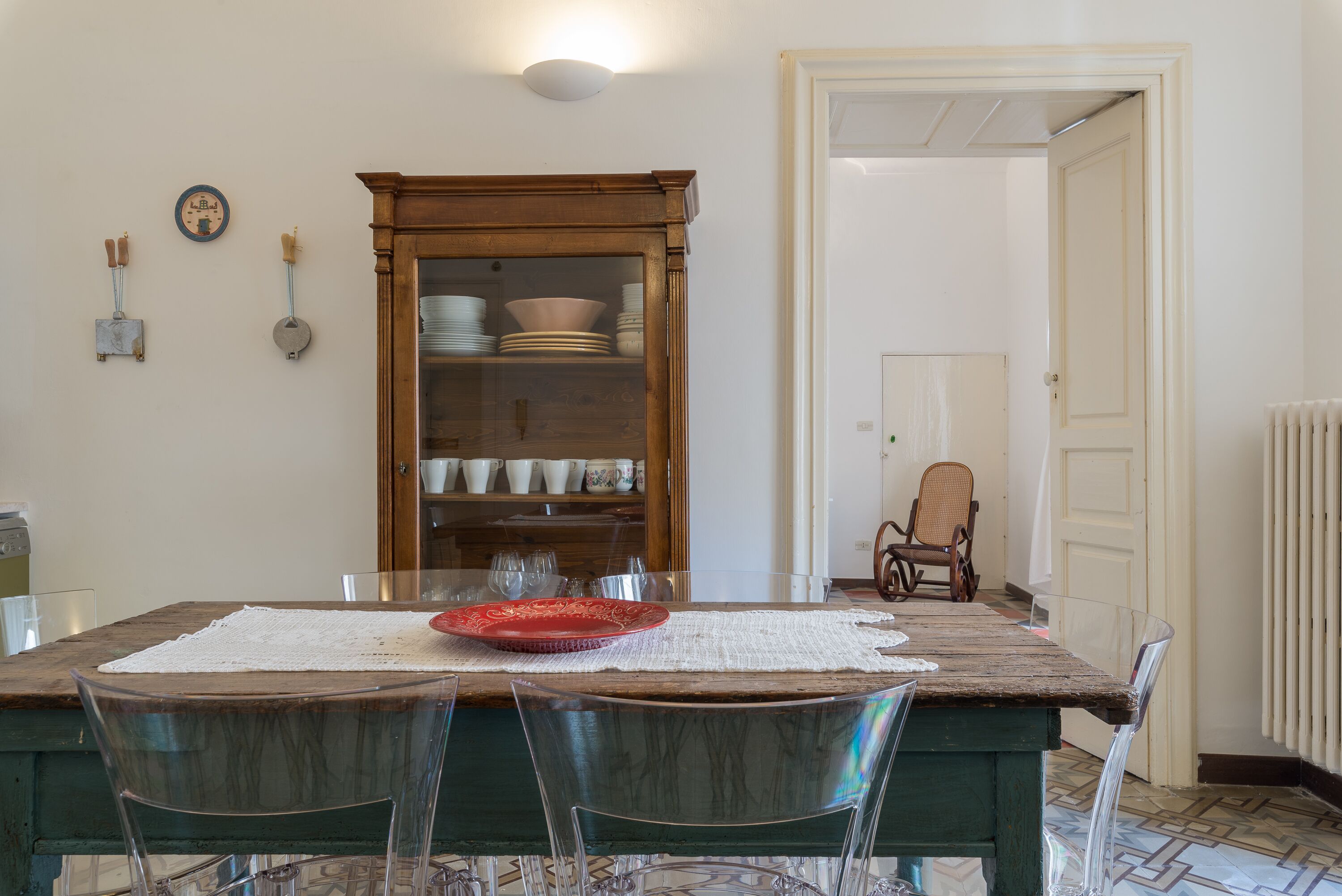Un coin repas avec une table en bois, des chaises transparentes, un buffet en verre contenant de la vaisselle et une chaise au fond.