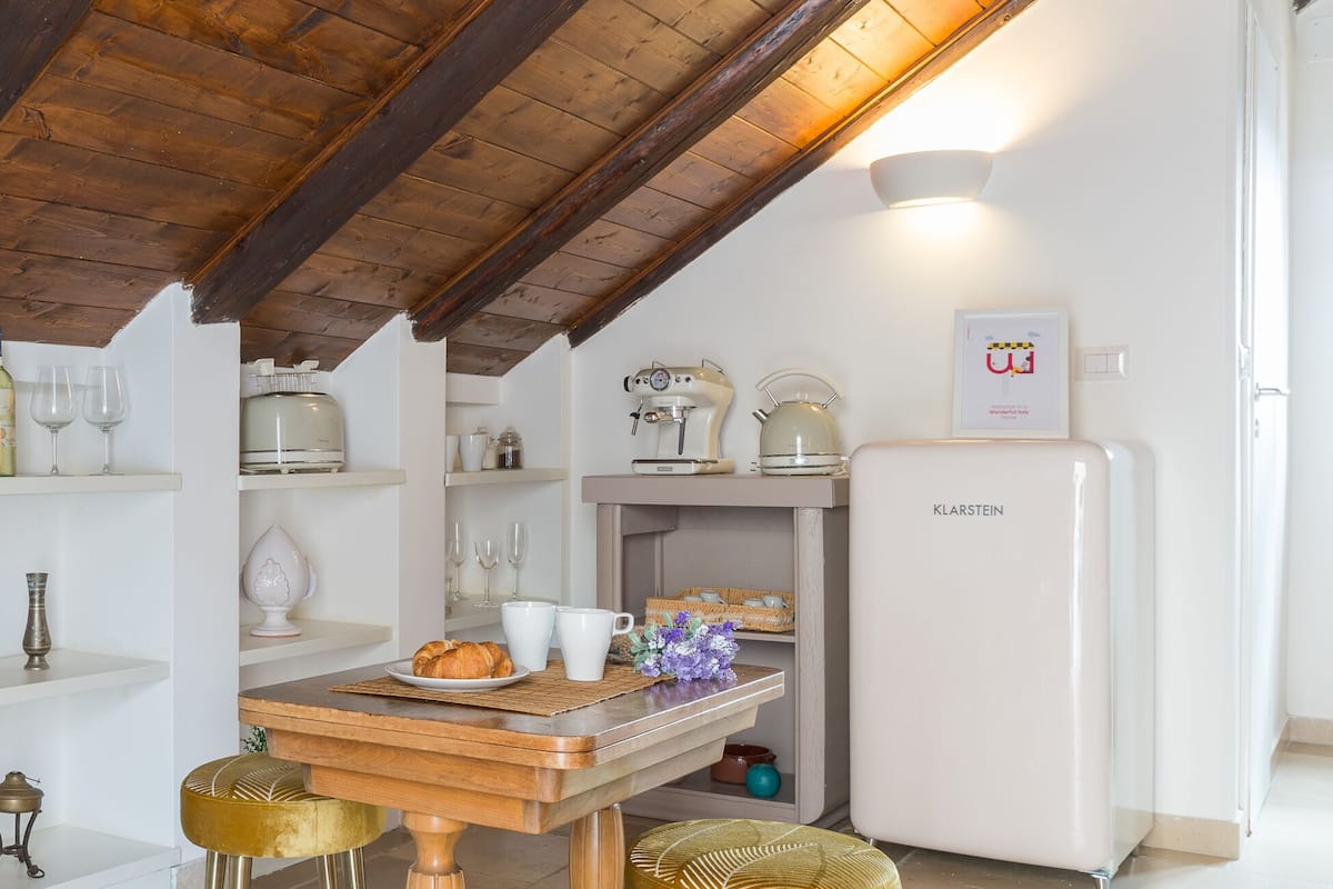 A cozy kitchen with wooden beams, a white refrigerator, and a table with stools.