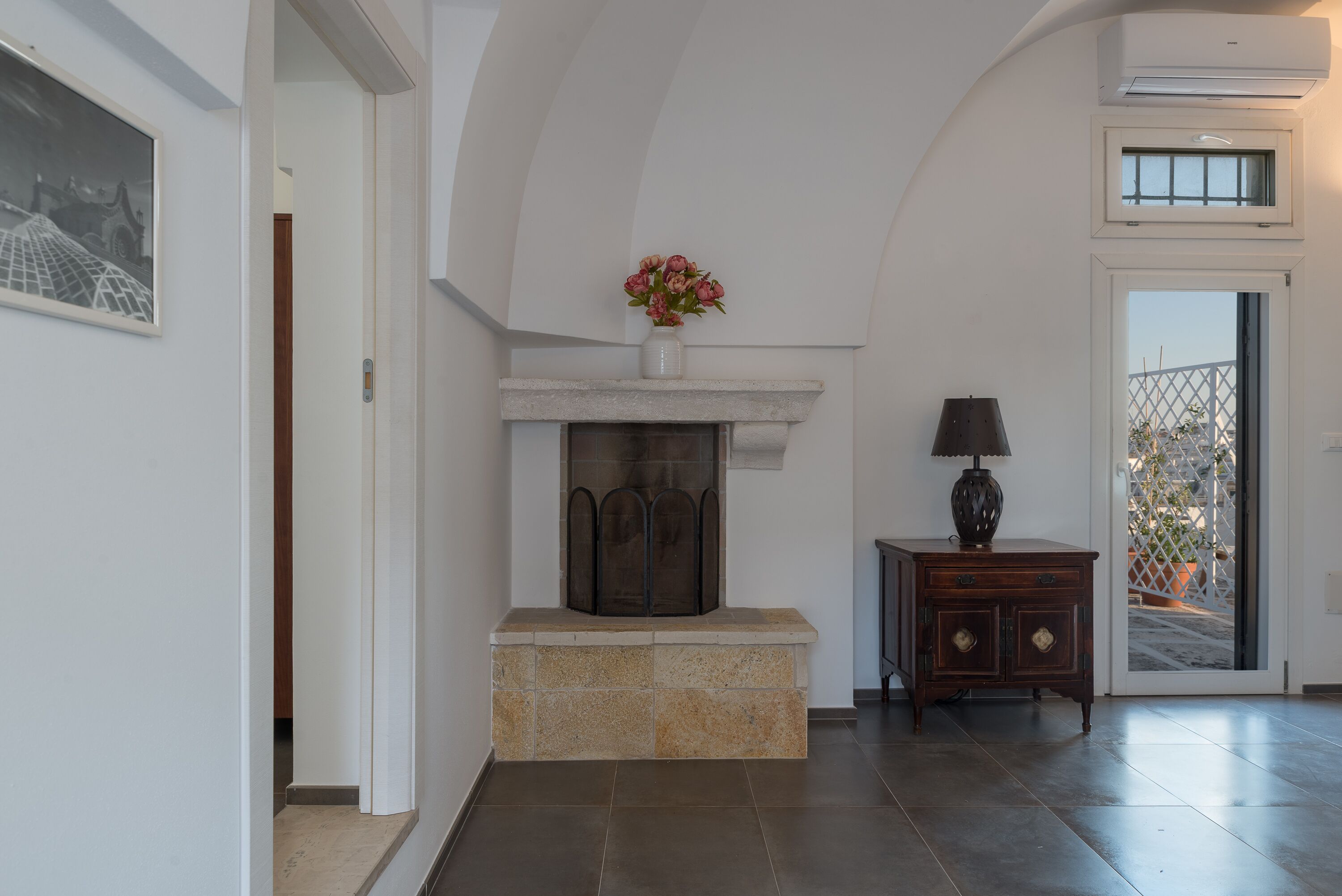 A hallway with a stone fireplace, a wooden cabinet, and a door leading to an outdoor area.