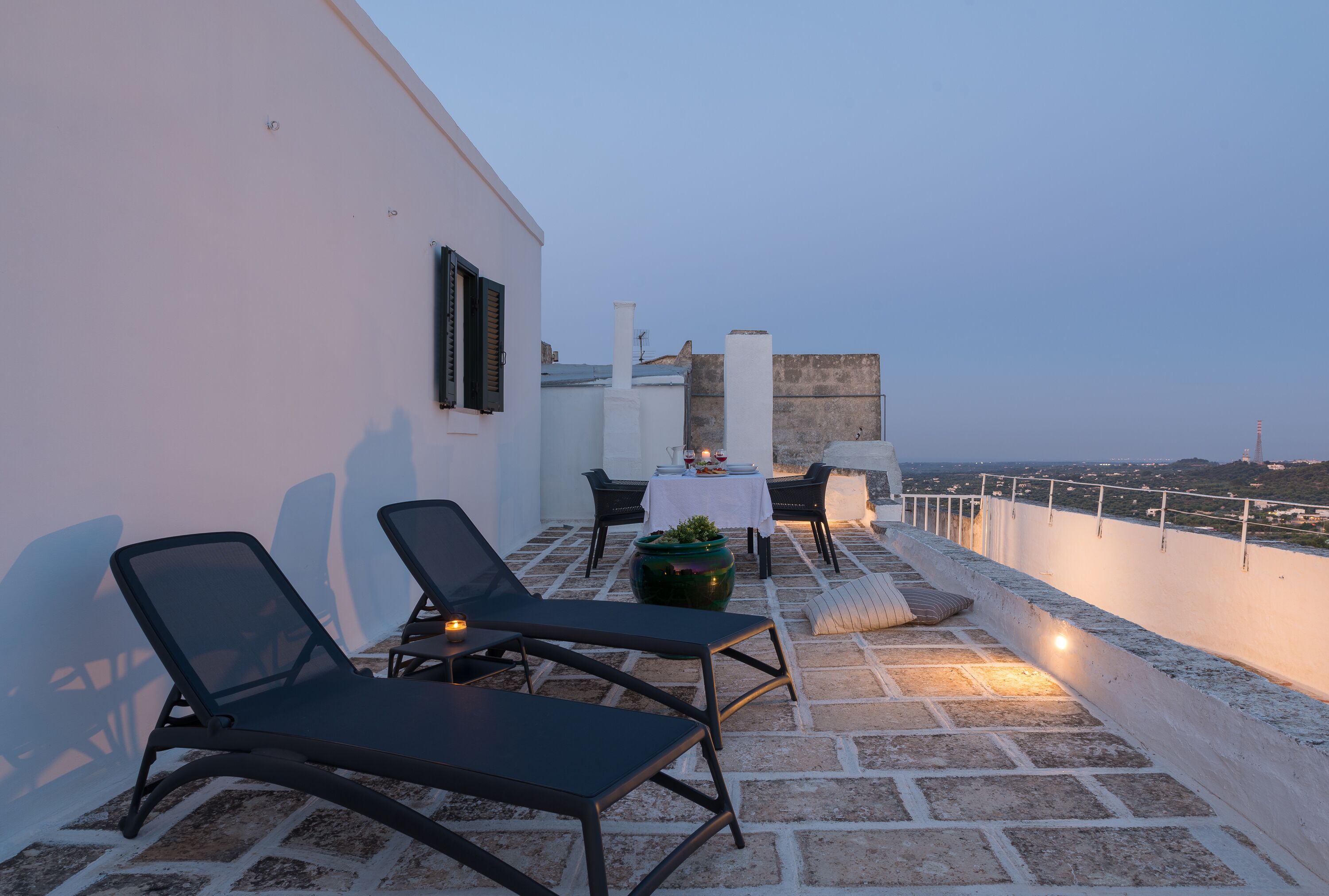 Eine Dachterrasse mit Liegestühlen, einem Tisch mit einer Vase und Blick auf die Stadtlandschaft.