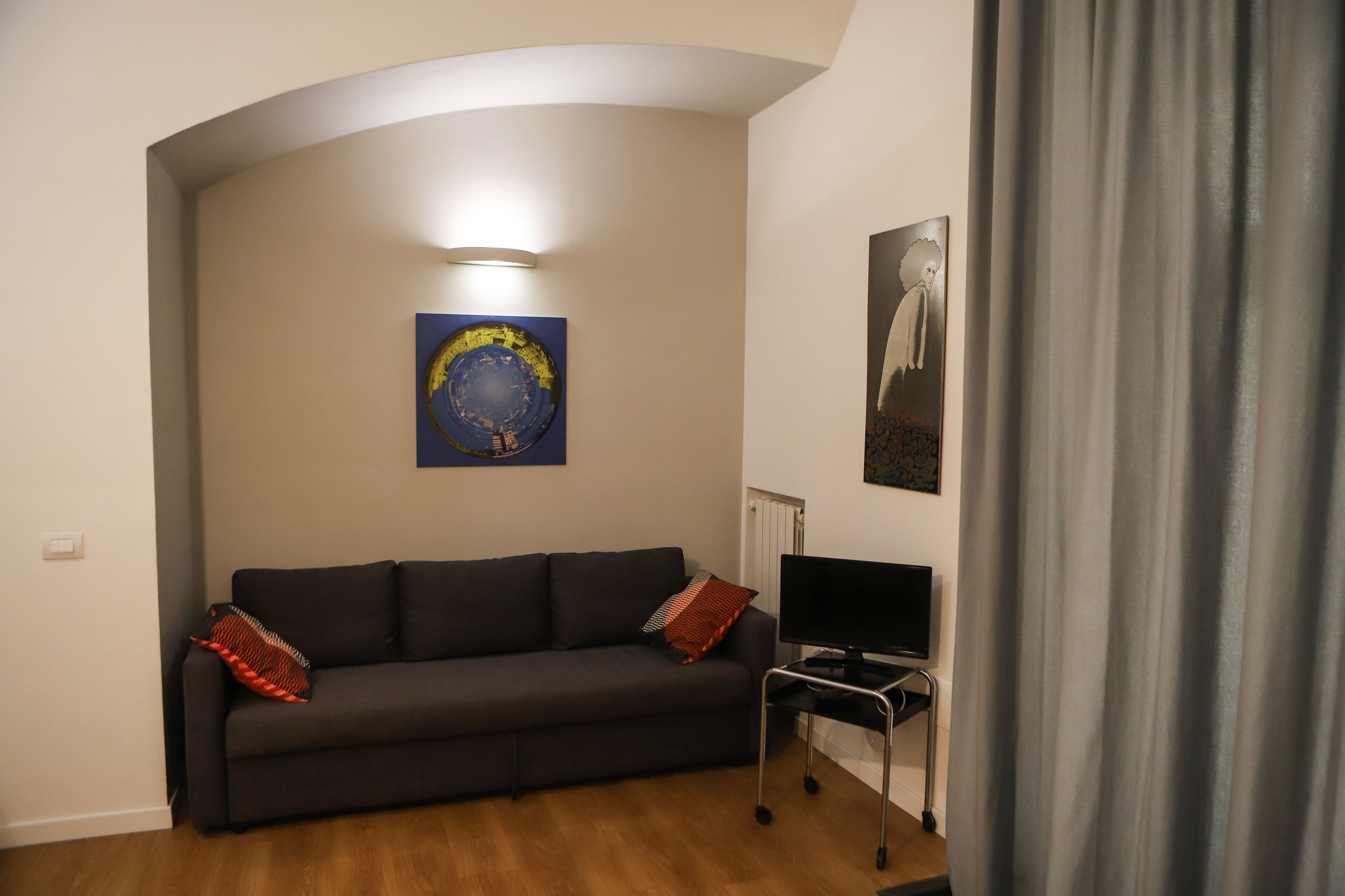 Een woonkamer met een donkere bank, een flatscreen televisie op een standaard en kunstwerken aan de wanden.