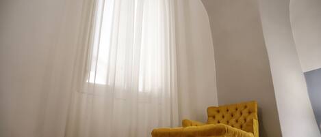 A yellow armchair in a room with a large window covered by sheer white curtains.