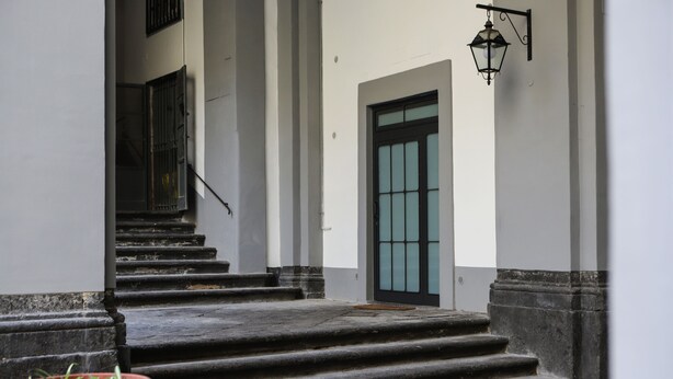A set of stone steps leading to a door with a glass panel, flanked by white walls and a black lantern.
