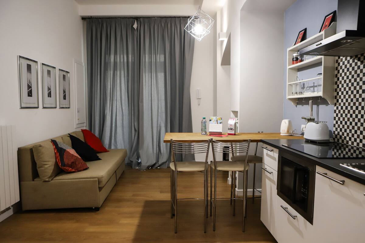 Een moderne keuken met een zithoek en een bank met kussens, plus een betegelde achterwand met ruitpatroon.