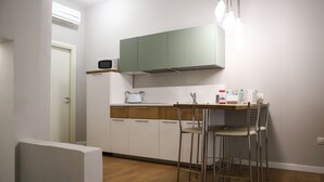 A compact kitchen with white cabinets, a microwave, and a small dining area with metal chairs.