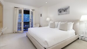 Une chambre avec un grand lit, une chaise, un bureau et un balcon avec des rideaux.